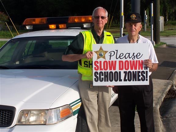 Volunteering Volunteers holding drive safe in school zone sign